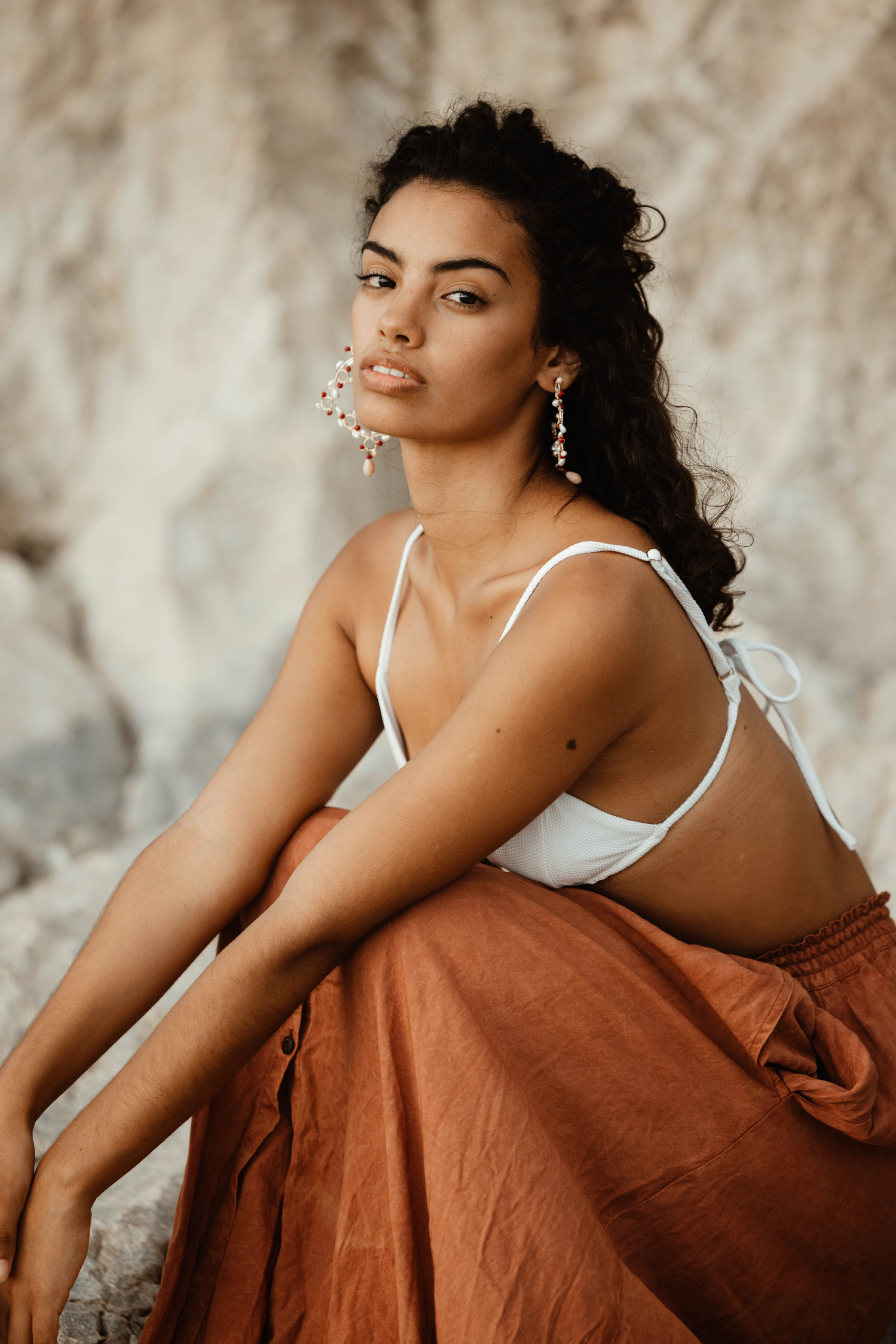 Woman in a white top and brown skirt sitting against a textured wall.