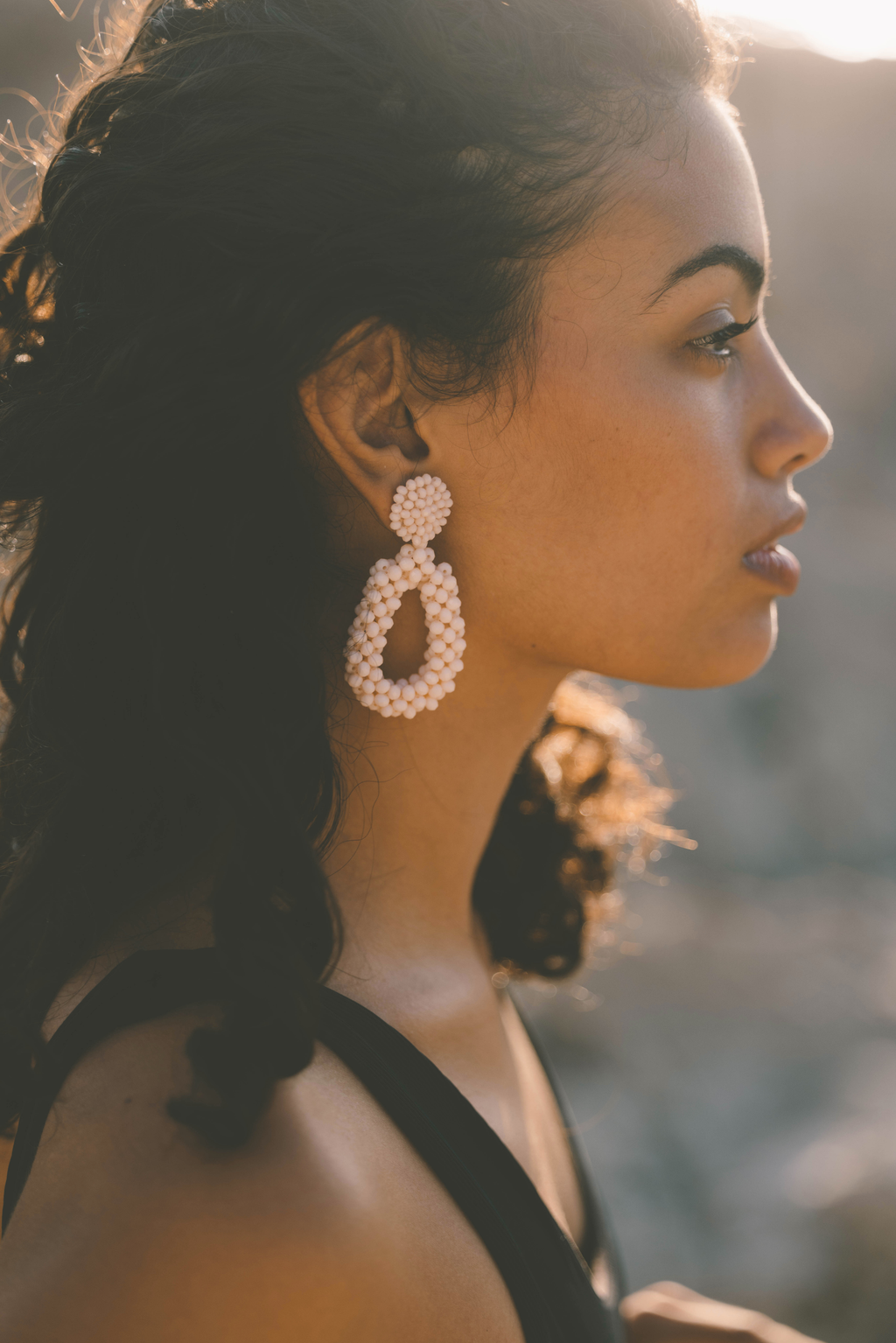 Woman wearing large pink beaded earrings with a blurred background