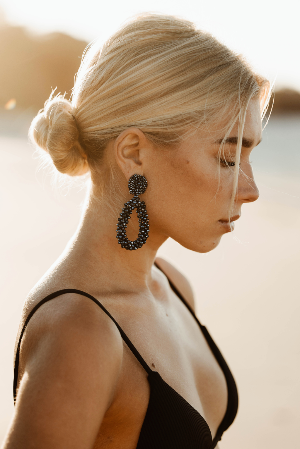 Woman wearing large black beaded earrings with a blurred background